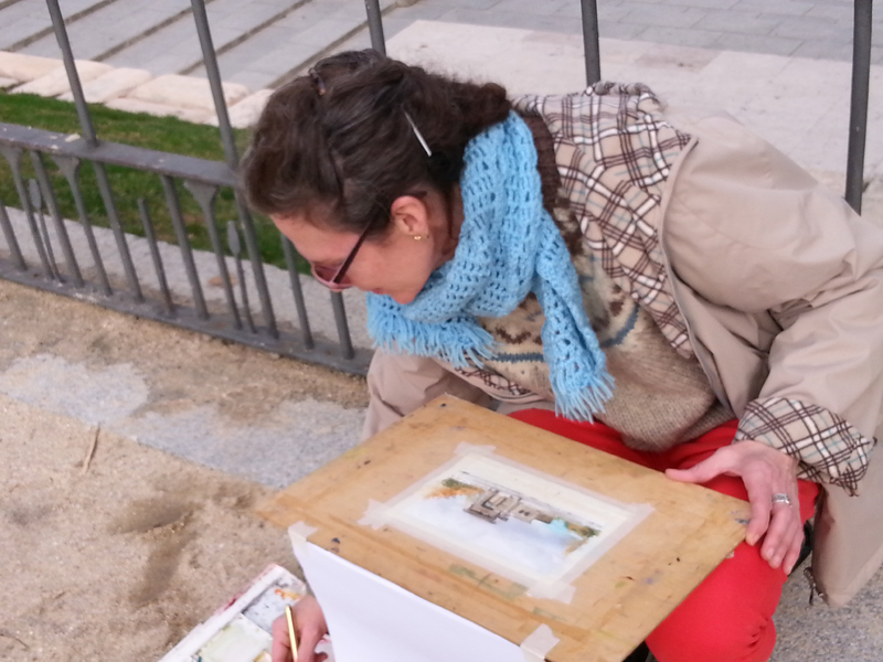 A picture of a woman mixing colors with her watercolor taped to a board on her lap.