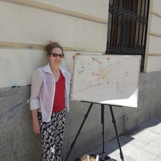 A woman standing next to an easel with the start of a watercolor.