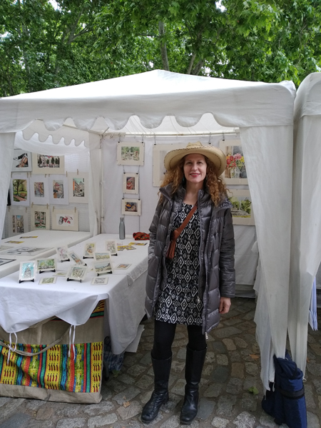 Lady with Hat standing in front of her art stand.